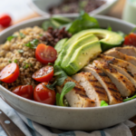 Salade protéinée complète au poulet grillé, avocat, quinoa et légumes frais dans un grand bol en bois, prête à être dégustée
