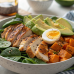 Bol de salade protéinée post-workout avec poulet grillé, patate douce, avocat, oeuf et épinards présenté sur un tapis de sport